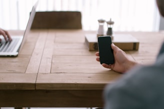 Close-up of hands holding a smartphone with accessories on a wooden table.