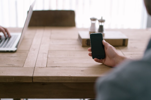 Close-up of hands holding a smartphone with accessories on a wooden table.