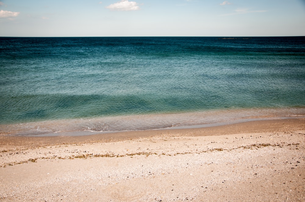 Ruhiges Wasser des Meeres unter blauem und weißem Himmel während der Tagesfotografie