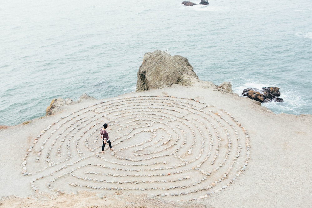 A person walking through a maze made out of rocks by the side of the beach
