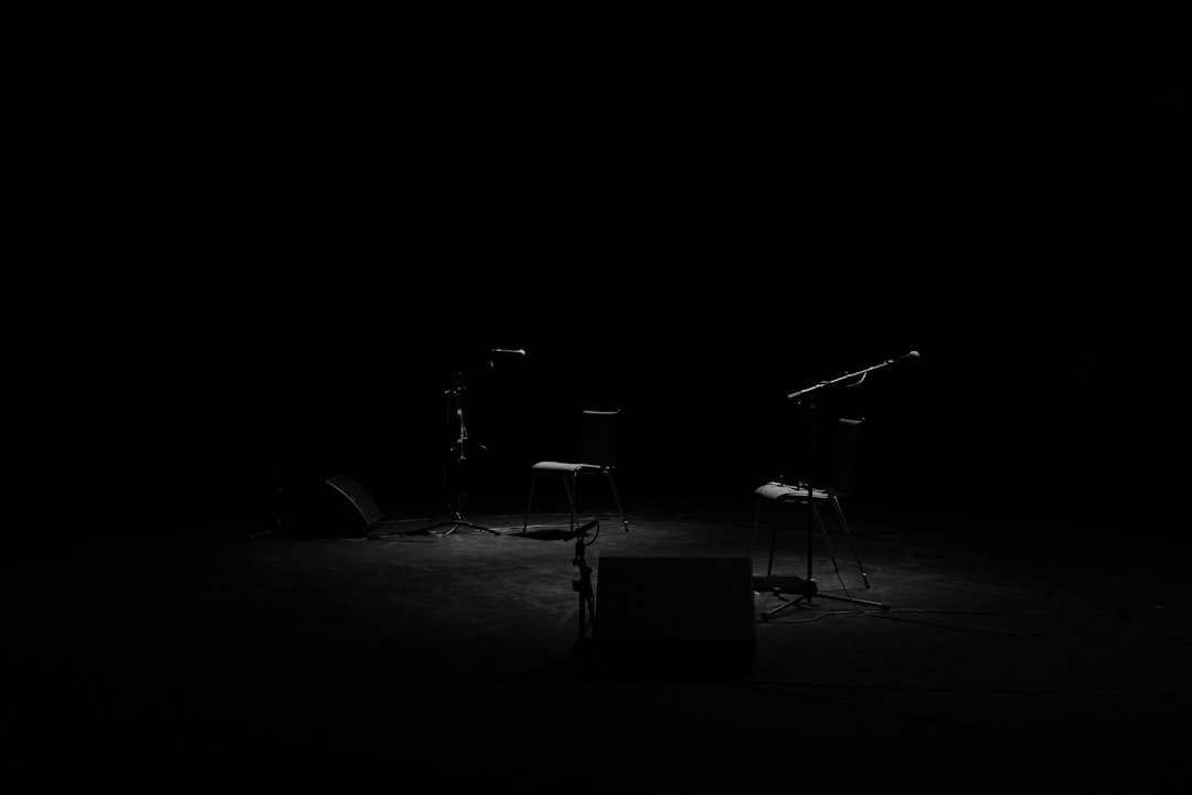 A dim shot of two chairs and microphone stands on an empty stage