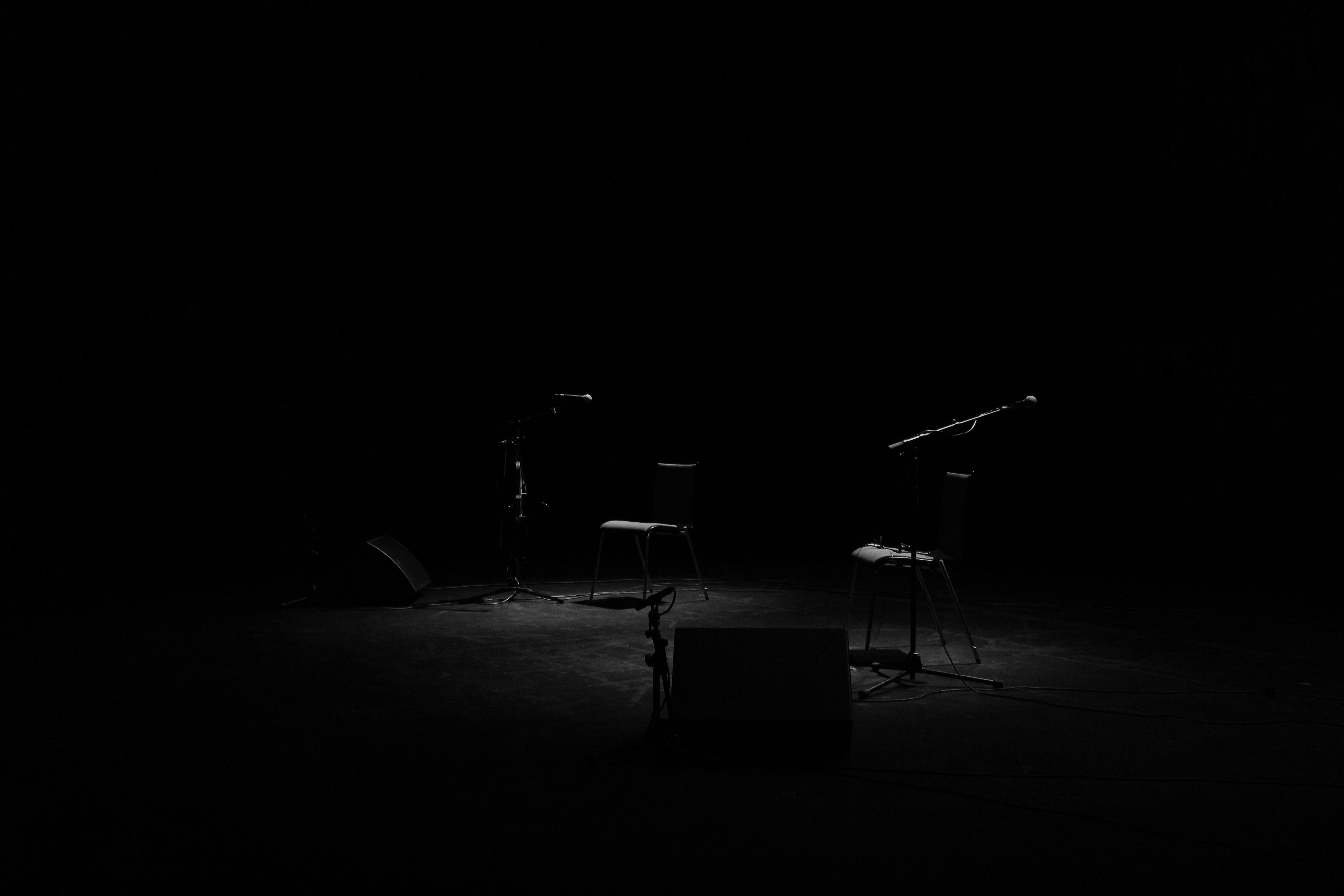 A dim shot of two chairs and microphone stands on an empty stage