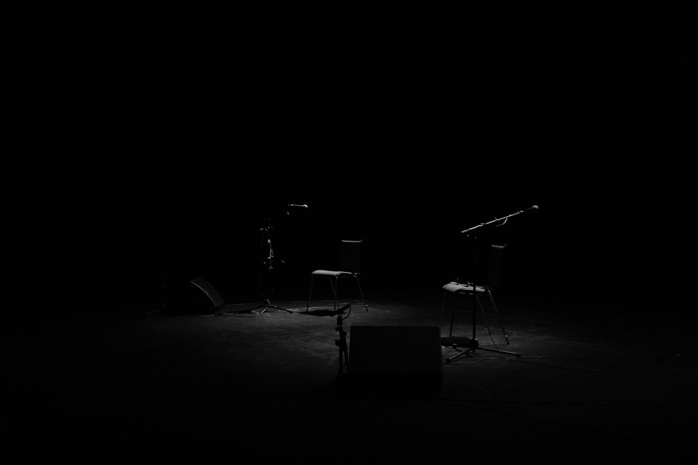 A dim shot of two chairs and microphone stands on an empty stage