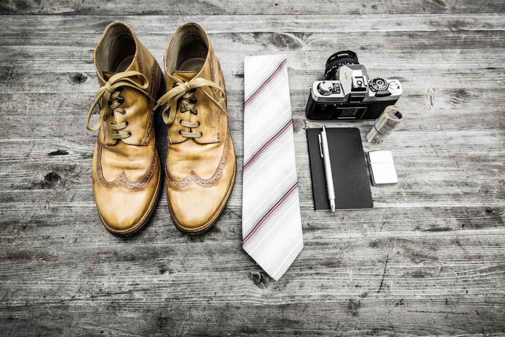 ネクタイの横に茶色の革のブーツ、ペン、ノートブック、MILCカメラ