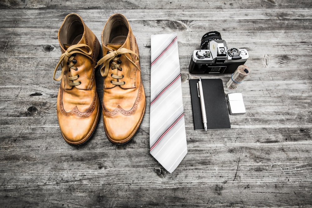 pair of brown leather boots beside necktie next to pen, notebook, and MILC camera