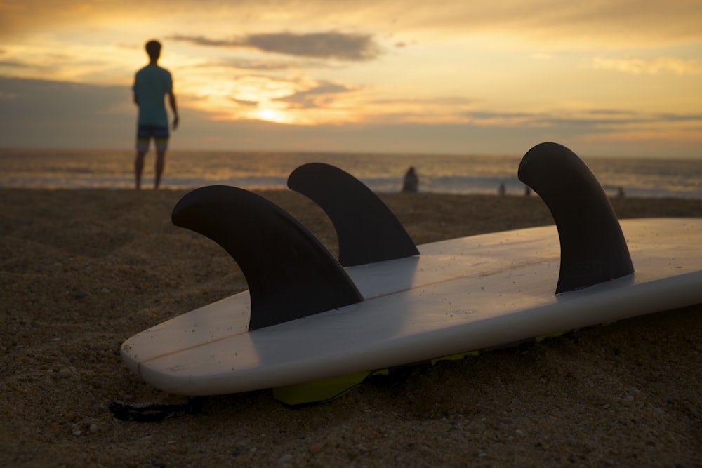 prancha de surf branca e preta na areia branca durante o pôr do sol