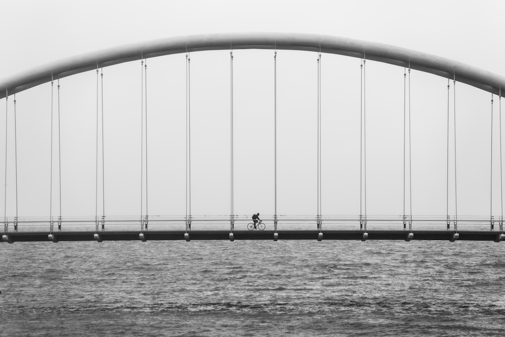 foto in scala di grigi di una persona che guida la bici sul ponte
