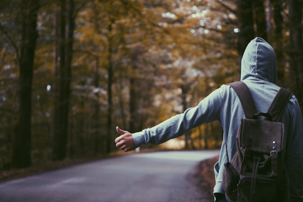 person standing beside road doing handsign