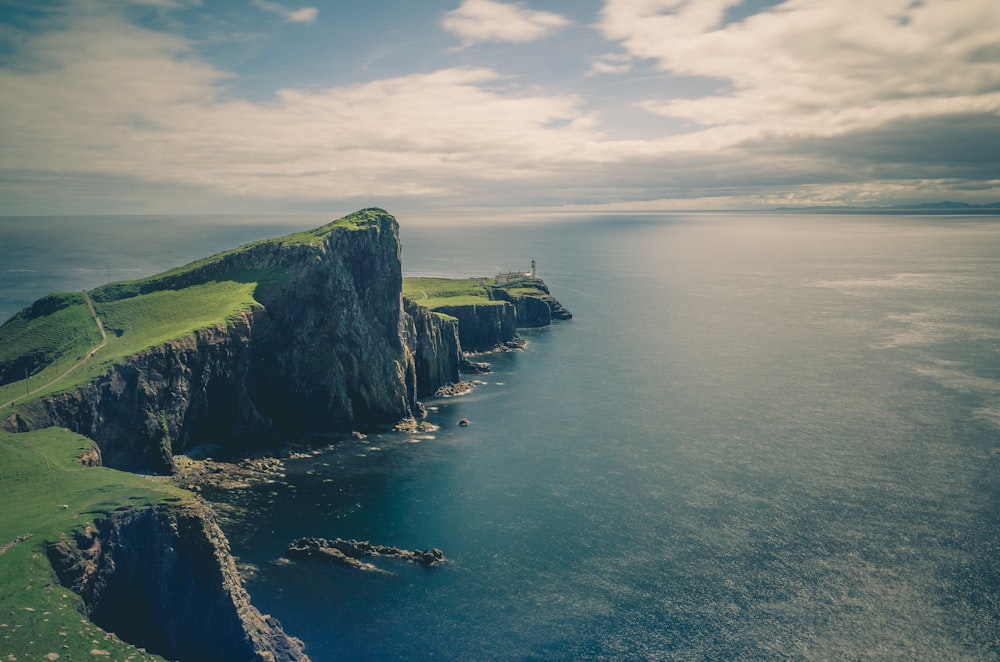 sea and rock cliff with grasses under cloudy sky