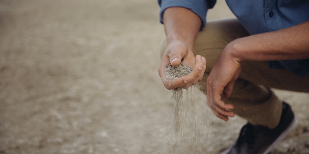 Person crouches down with a handful of sand that slips through their fingers