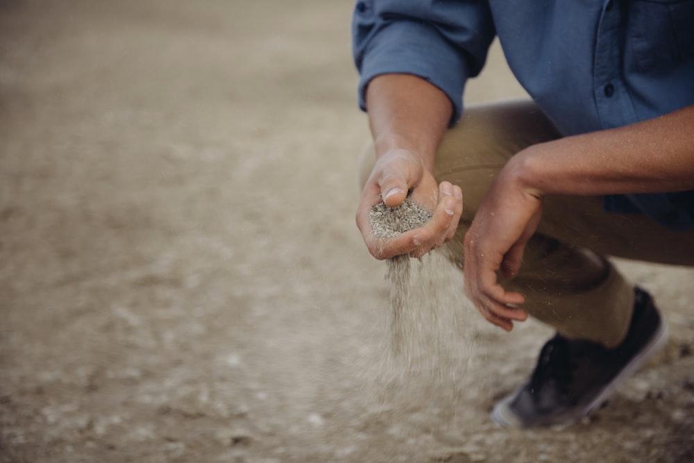 Pessoa se agacha com um punhado de areia que escorrega pelos dedos