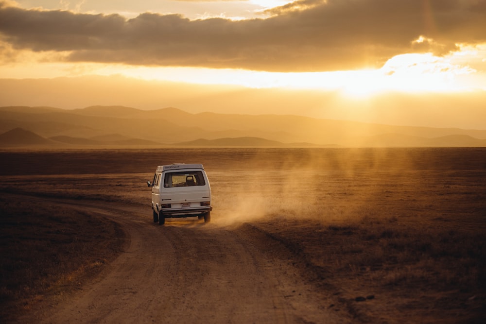 Vehículo blanco que viaja por el campo de tierra del desierto durante la puesta del sol