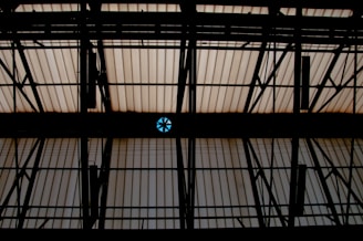 A ceiling with dark, silhouetted metal framework and translucent panels. A singular circular vent with blue panels is visible against the predominantly beige translucent roofing.