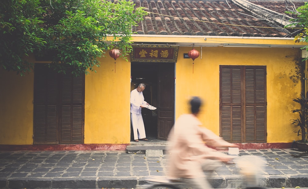 Casa asiática con un hombre en la puerta y otro hombre en bicicleta pasando