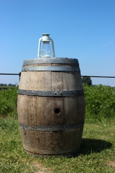 A rustic rainwater collection barrel set up beside a simple wooden shed under a bright blue sky.